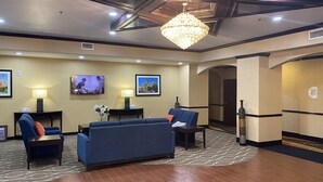 A hotel lobby with a large blue sofa, a chandelier, framed pictures on the walls, and a television. - Comfort Suites Lake Worth (Fort Worth)