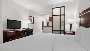 Ein Hotelzimmer mit einem Bett, einem Schreibtisch mit Fernseher, einem Sessel, einem Nachttisch mit Lampe und einem Spiegel.