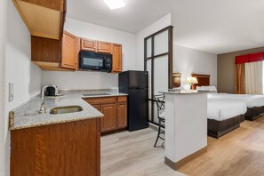 A compact hotel room with a kitchenette, a bed, a small table, and a chair.