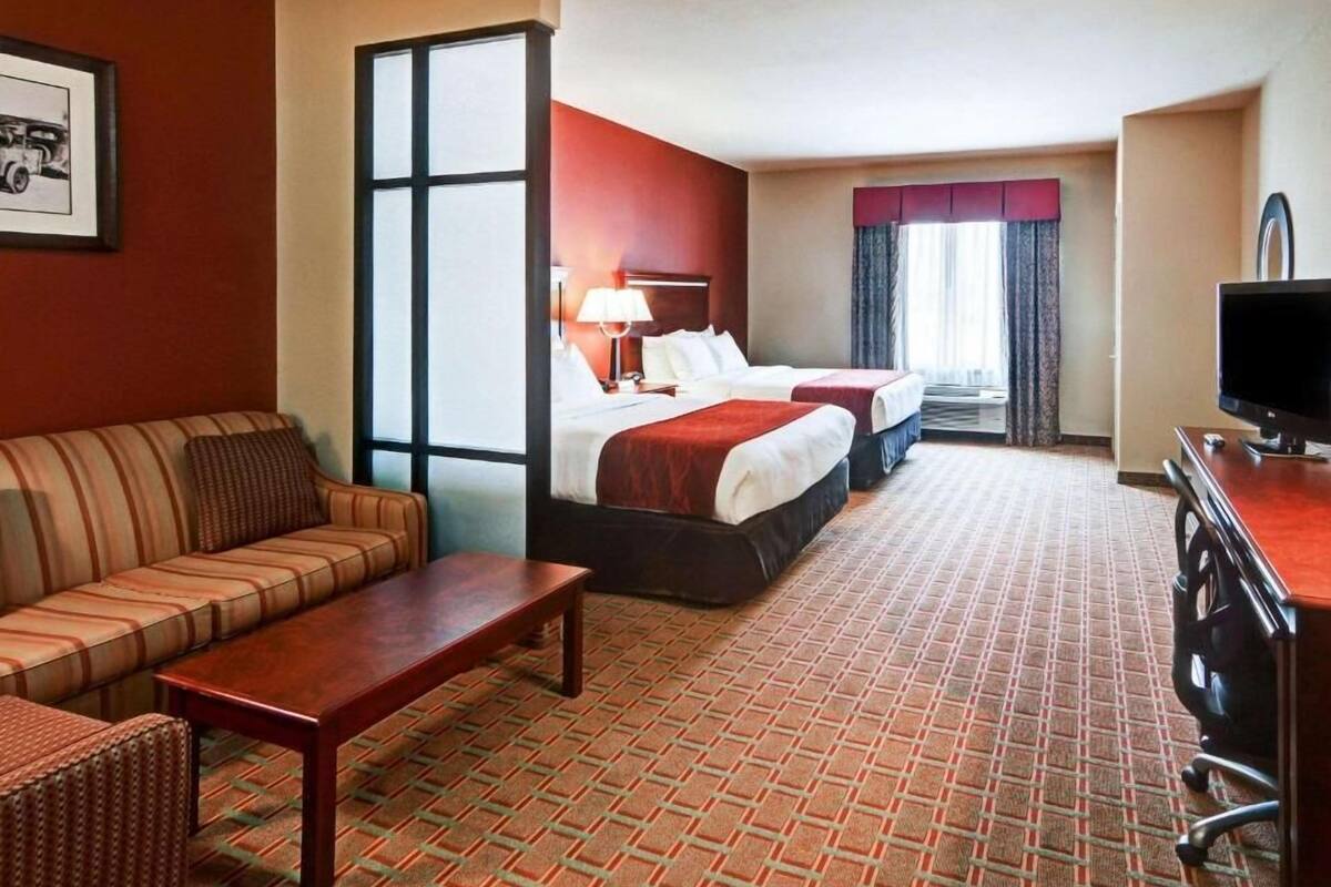 Ett hotellrum med en soffa, två sängar, en TV och ett stort fönster.