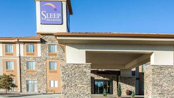 A Sleep Inn & Suites building with a stone facade, multiple windows, and a covered entrance area.