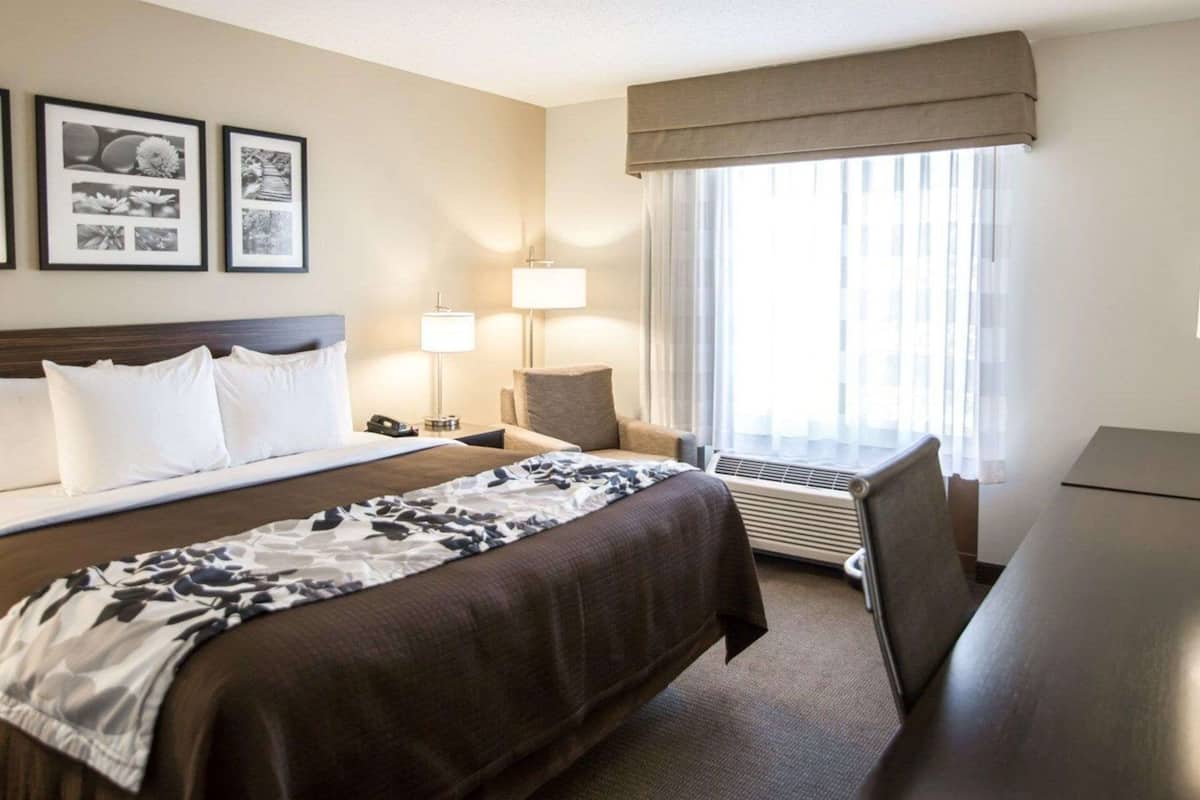 A hotel room with a large bed, two bedside tables with lamps, a desk, and a window with curtains.