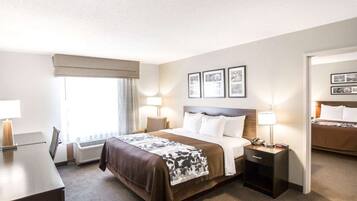 A hotel room with a large bed, bedside tables, a desk, and a chair. There are framed pictures on the wall and a window with curtains.