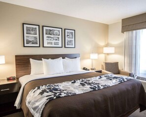 A hotel room with a large bed, two bedside tables, a chair, and a window with curtains. There are three framed pictures on the wall above the bed.