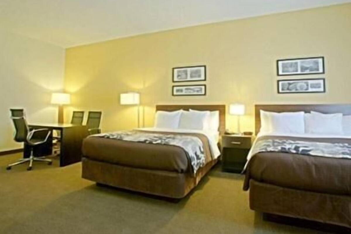 A hotel room with two beds, a desk, and two lamps.