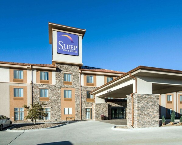 A Sleep Inn & Suites building with a stone facade, multiple windows, and a clear blue sky.