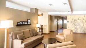 A modern hotel lobby with a beige sofa, armchairs, a small round table, and a lamp. - Sleep Inn & Suites Norton (Norton)