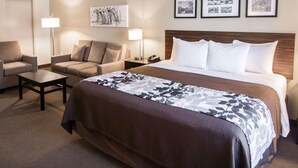 A hotel room with a bed, two armchairs, a small table, and a nightstand. There are three framed pictures on the wall above the bed. - Sleep Inn & Suites Norton (Norton)