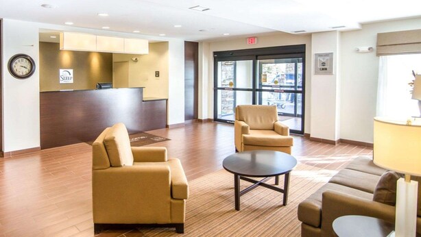 A lobby with a reception desk, two armchairs, a small table, and a clock on the wall. - Sleep Inn & Suites Norton (Norton)