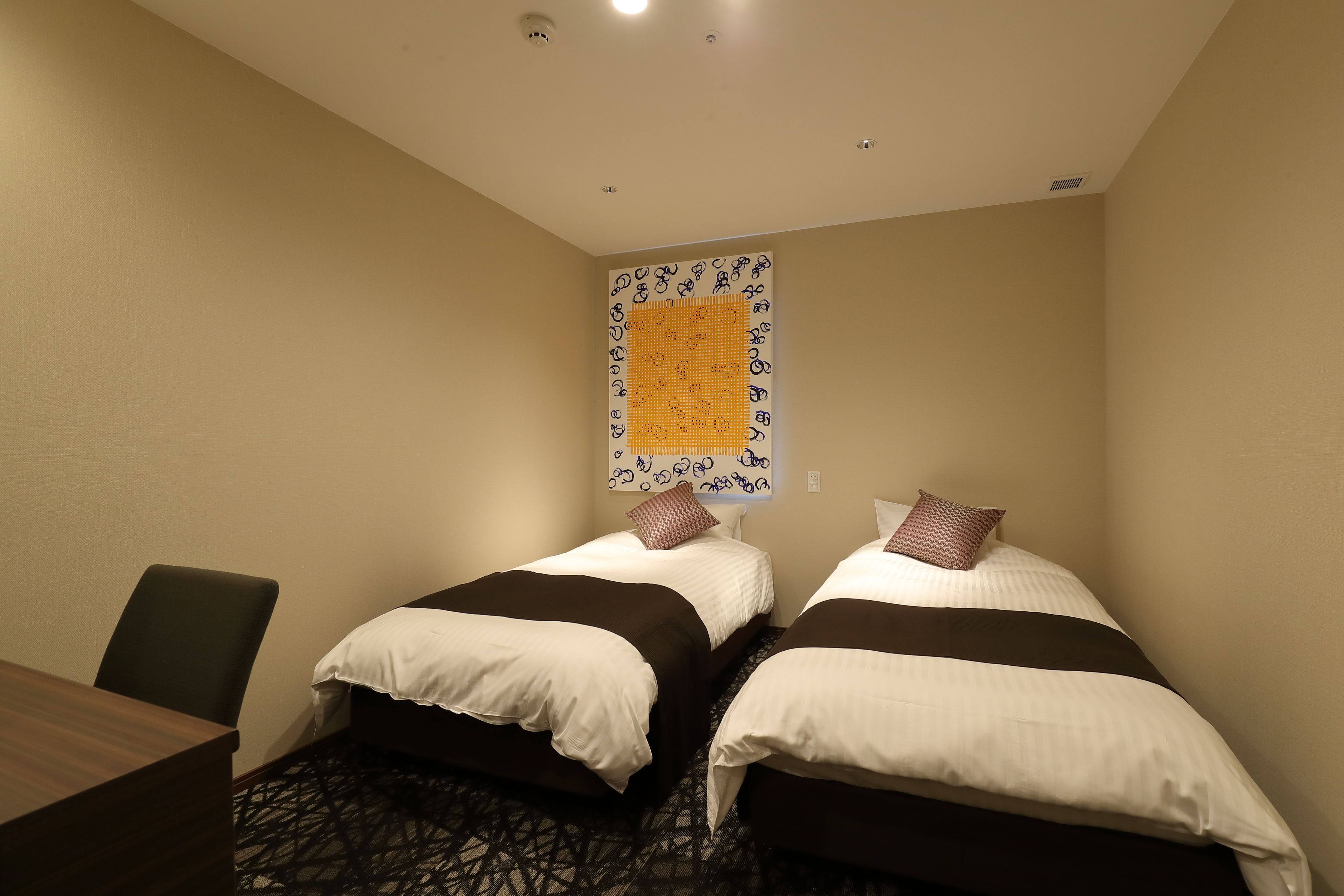 A hotel room with two beds, a desk, and a patterned carpet.