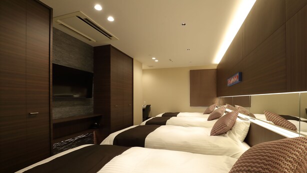 Una habitación de hotel con tres camas, un televisor de pantalla plana, un espejo grande y un armario de madera.