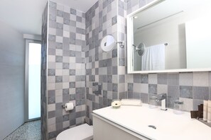 Un bany amb parets de rajola graella, un lavabo blanc amb mirall i un vàter.