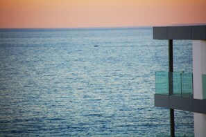 Vista del mar amb un vaixell a la distància i un edifici modern amb balcons de vidre.