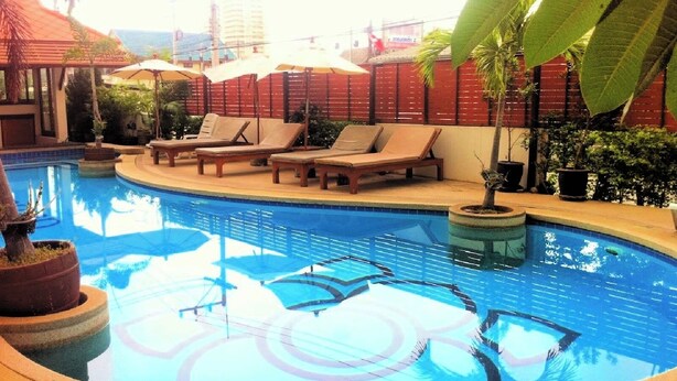 A pool area with lounge chairs and umbrellas, surrounded by potted plants and a red building in the background. - LaOr Inn Hua Hin (Hua Hin)