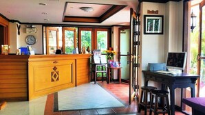 A reception area with a wooden counter, a desk with a computer, and a chair. - LaOr Inn Hua Hin (Hua Hin)