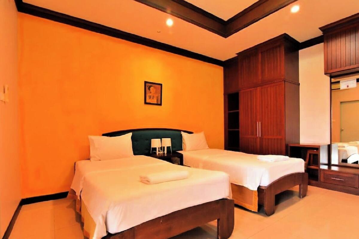 A hotel room with two beds, wooden headboards, a large wardrobe, and a mirror.