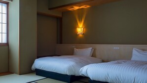 Et hotelværelse med to senge, en vægmonteret lampe og tatamimåtter.