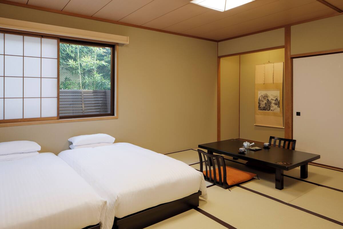 A room with two beds, a table with chairs, and a sliding door with a picture.