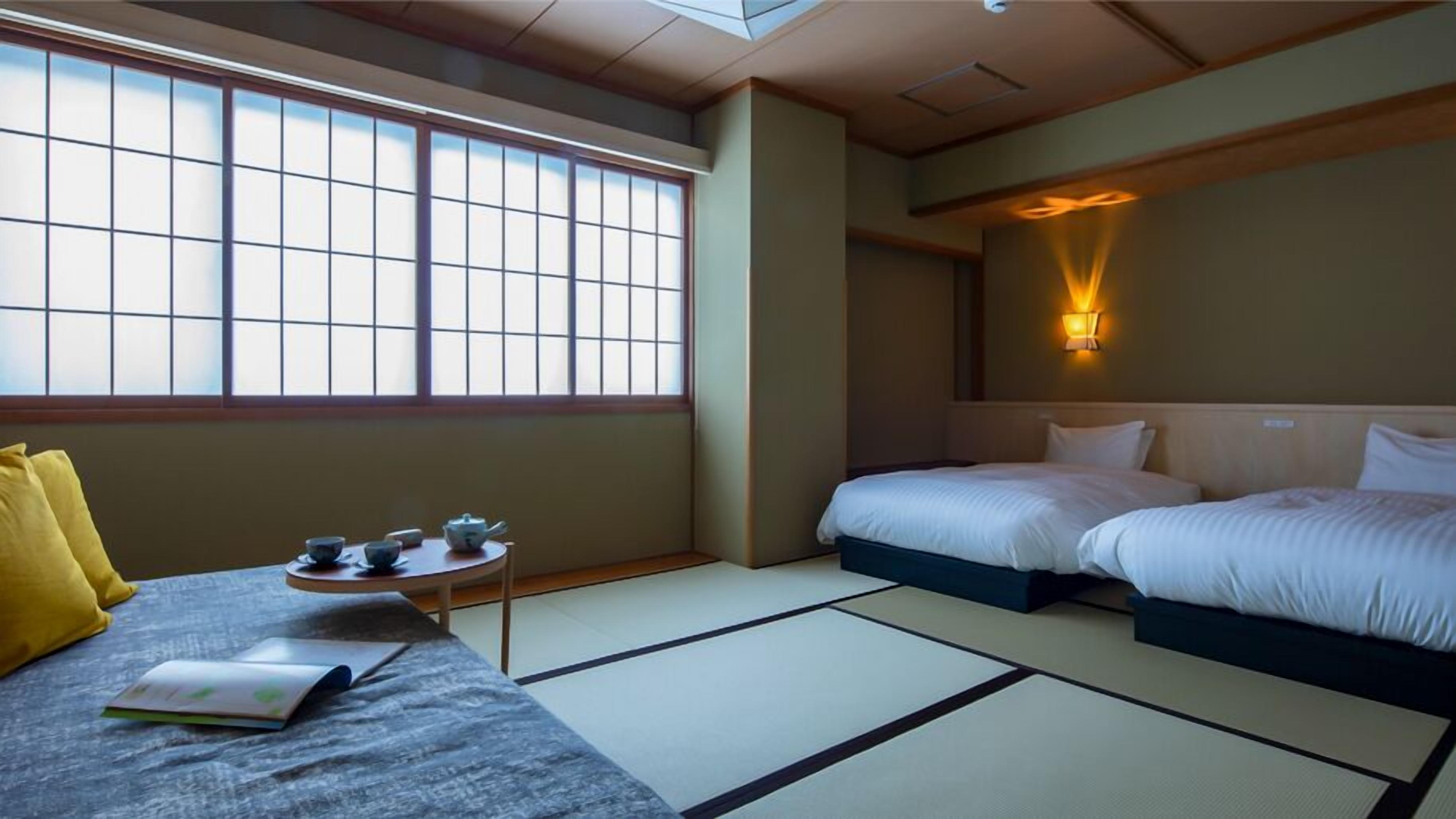 A hotel room with tatami flooring, a bed, a sofa, a small table with tea set, and a wall-mounted light.