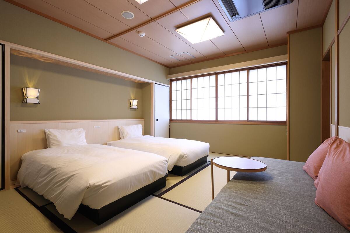 A hotel room with two beds, a small round table, and a large window.