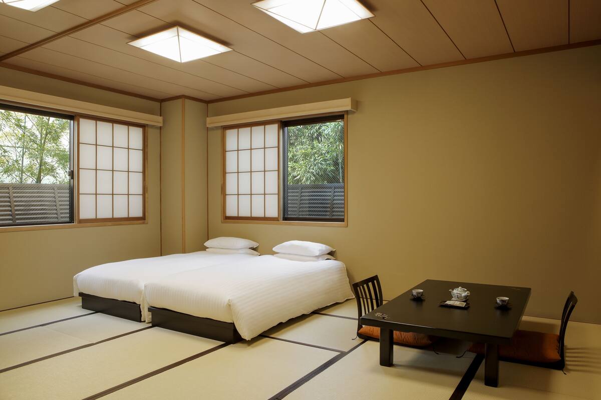 A traditional Japanese-style room with tatami flooring, a bed with white bedding, a table with a tea set, and sliding shoji doors.