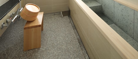 A bathroom with a bathtub, a wooden stool, and a shower area.