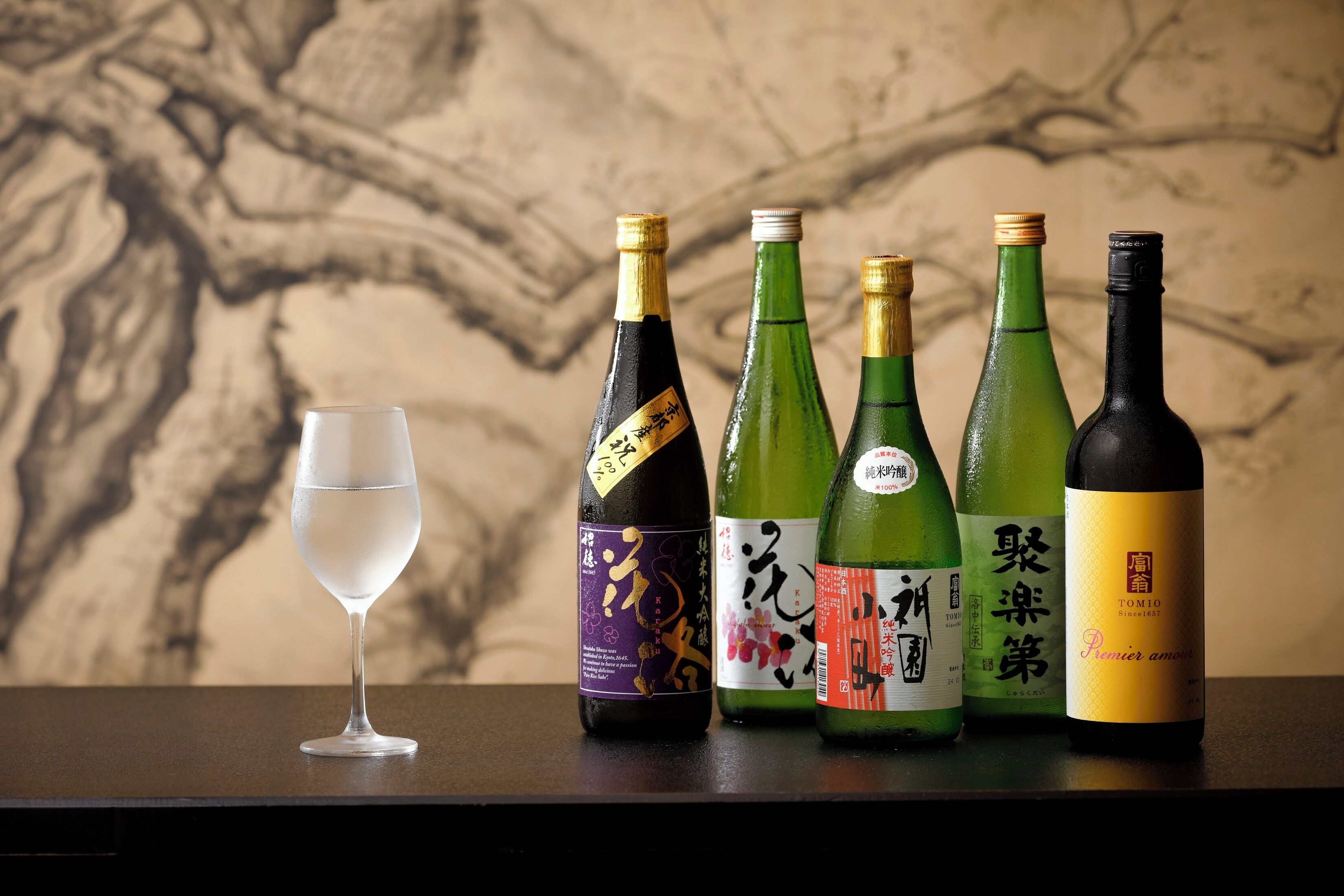 A glass of water and four bottles of Japanese sake on a table.