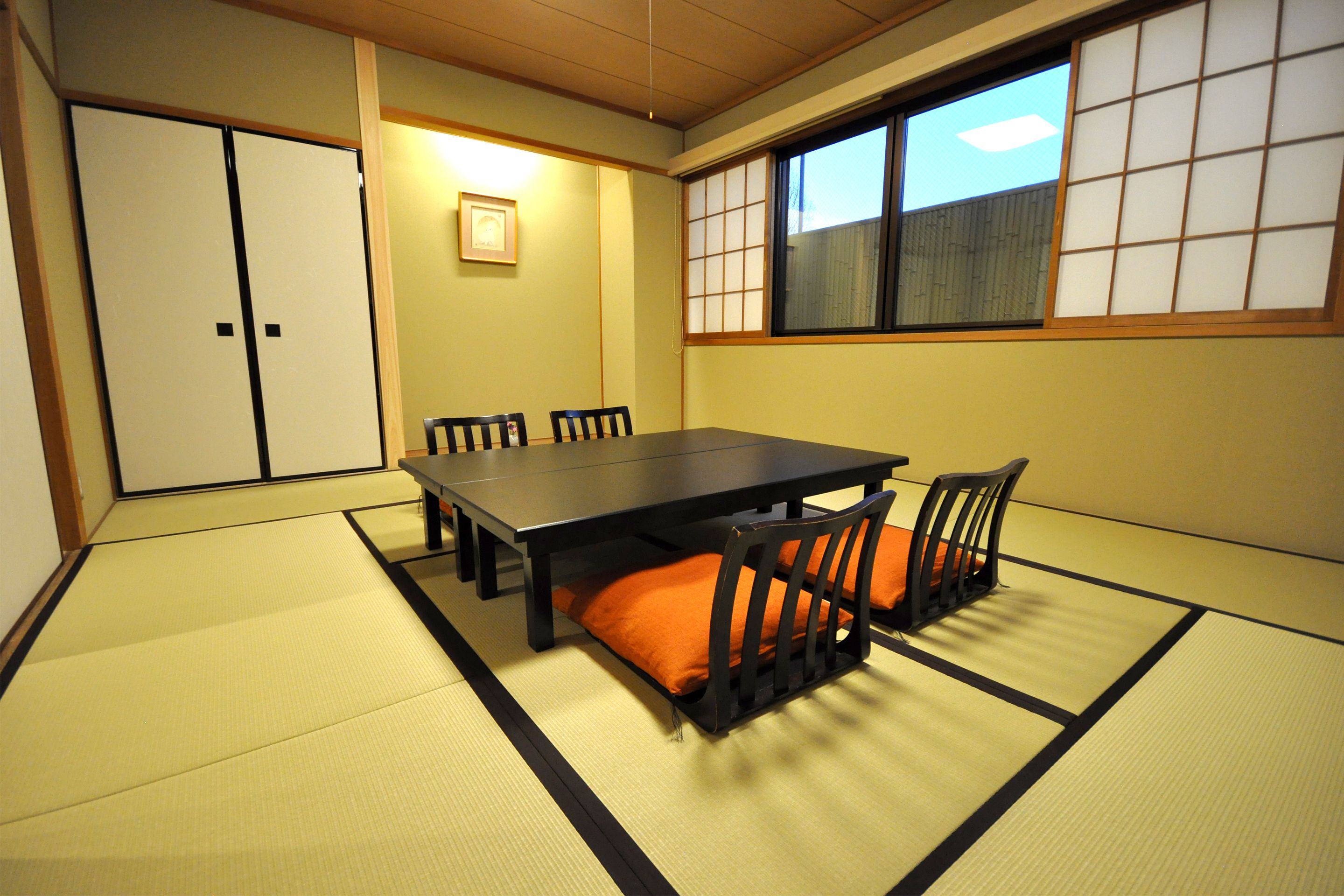 Una habitación japonesa tradicional con suelo de tatami, una mesa baja y sillas negras con cojines naranja.