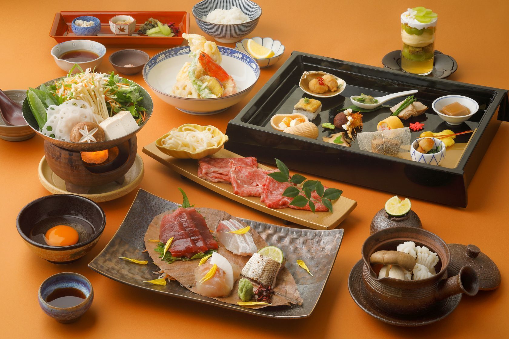 A variety of Japanese dishes and utensils on a table, including sushi, sashimi, and a hot pot.