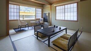 Et traditionelt japansk værelse med tatamimåtter, et lavt bord med puder og store vinduer med udsigt til en have og bjerge.