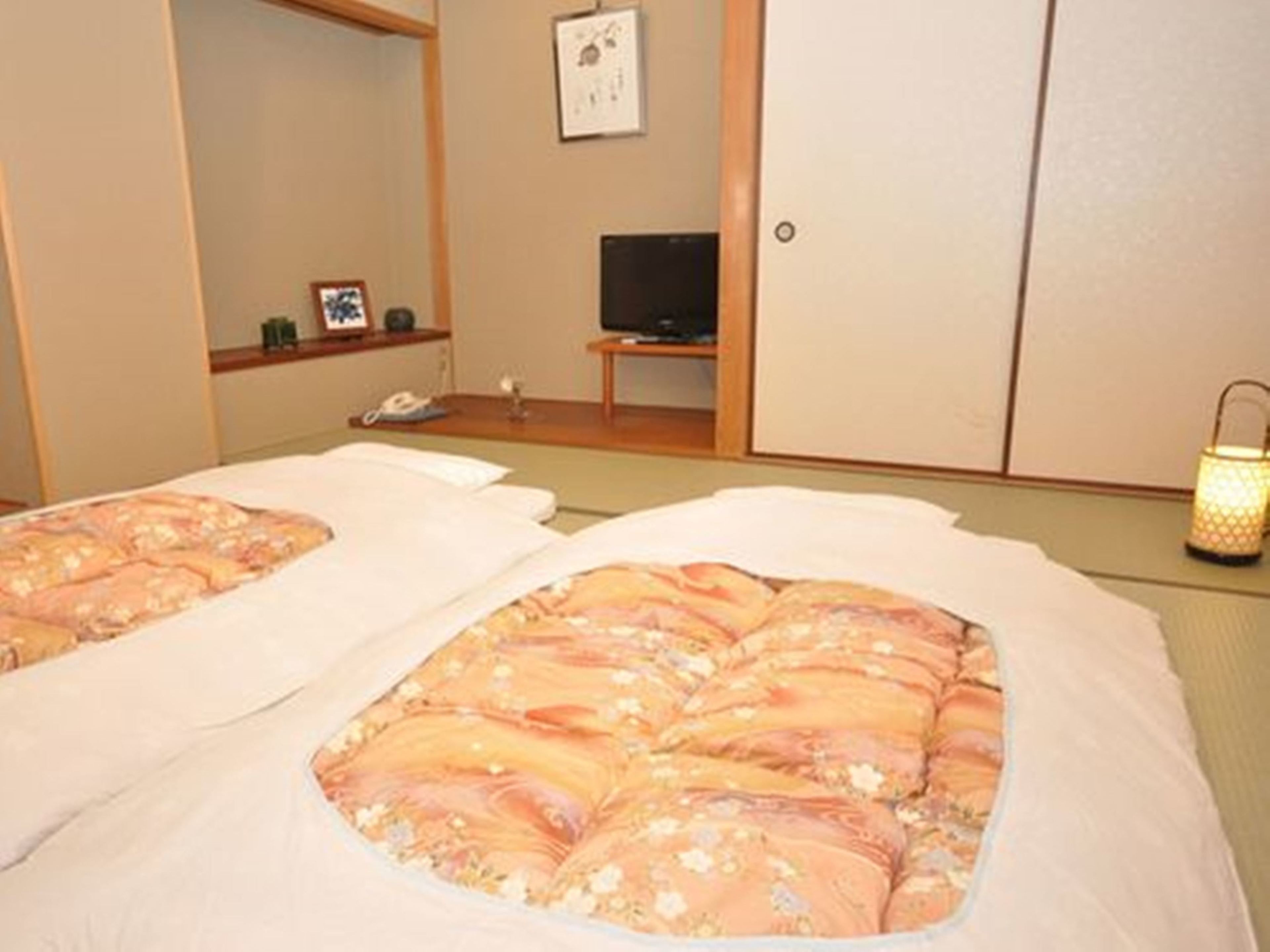 Habitación con dos camas, cada una con cubrecama floral, un televisor, una mesita y un teléfono en la pared.