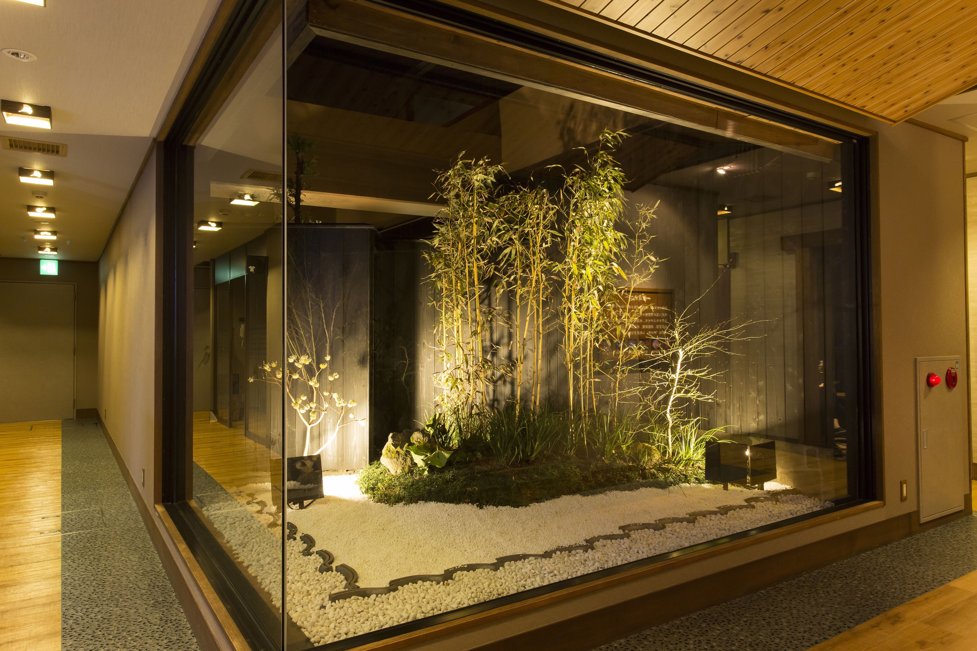 Un interior moderno con un cerramiento de vidrio que alberga un jardín de bambú, suelo de madera y una salida de emergencia visible.