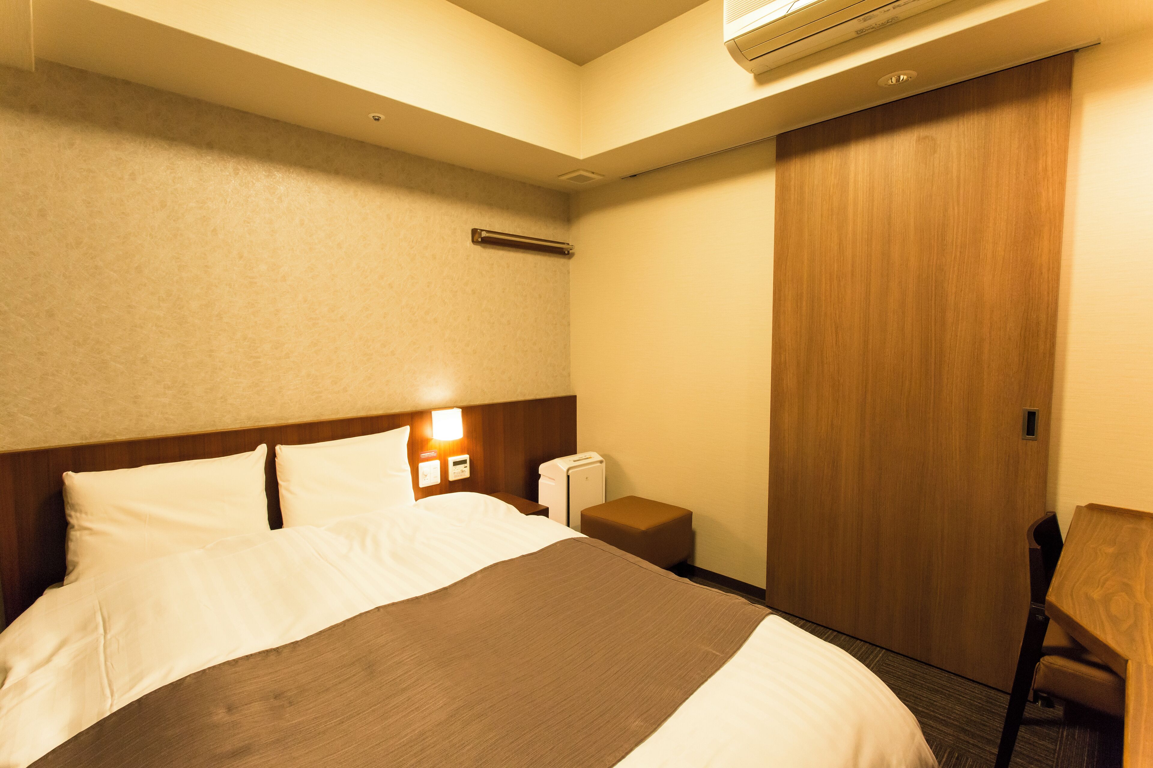 A hotel room with a bed, bedside table, nightstand, and a wooden wardrobe.
