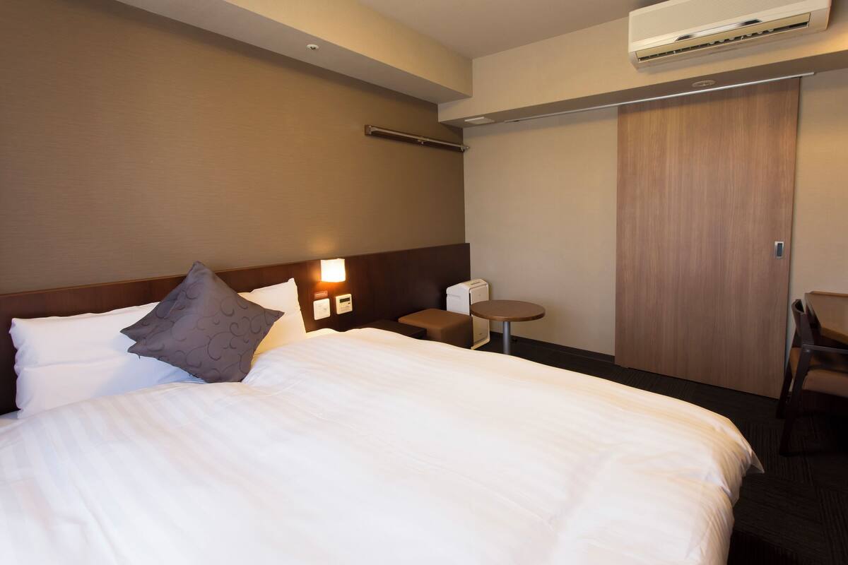Hotellihuone, jossa on suuri sänky, yöpöytä, tuoli ja vaatekaappi.