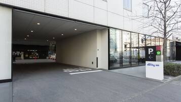 A hotel entrance with a covered parking area, a sign indicating a parking space, and a building with a tiled facade.