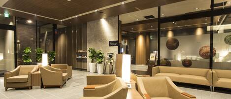 A modern lobby with leather sofas and armchairs, a reception desk, and decorative elements like plants and wall art.