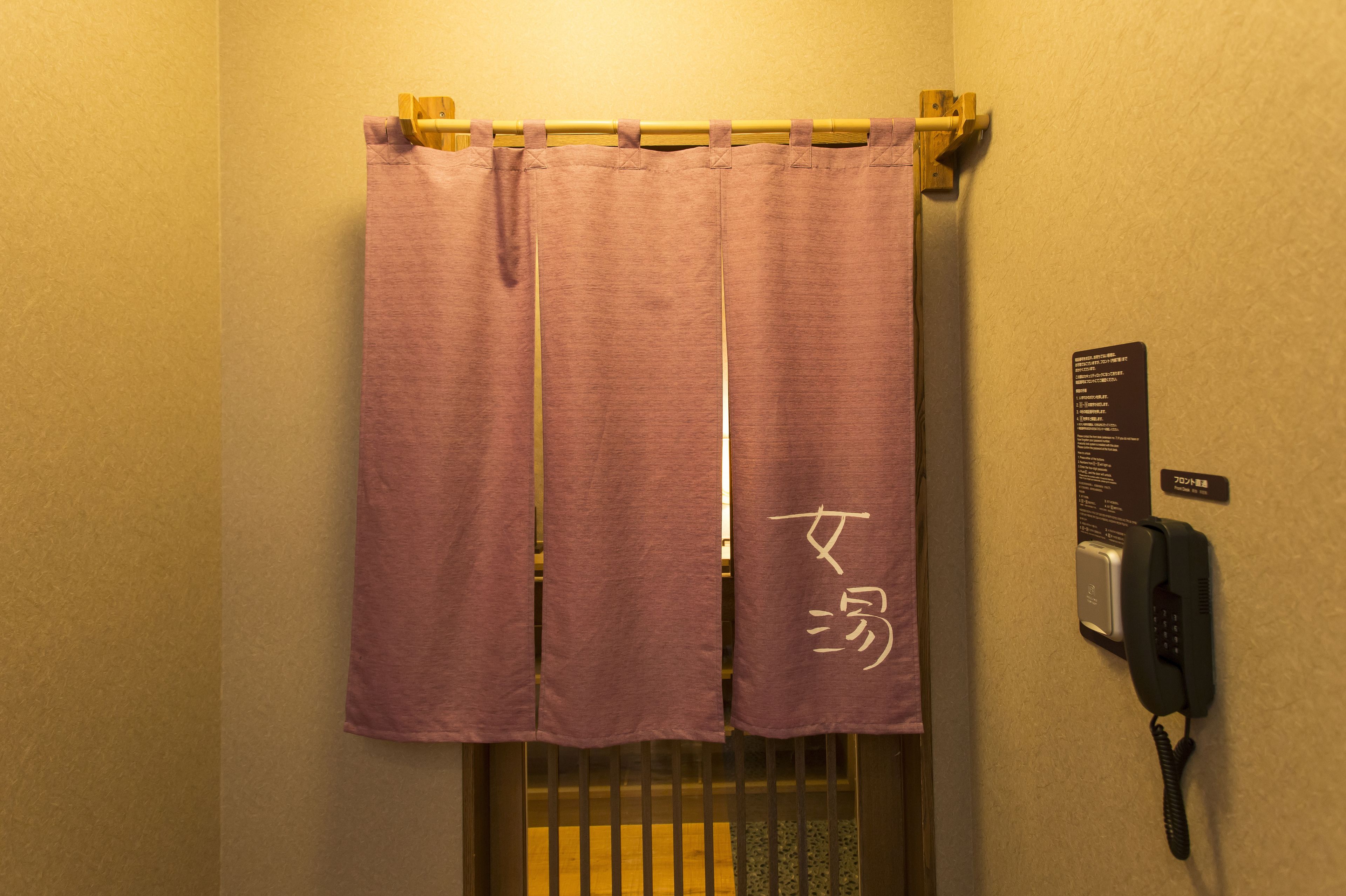 A bathroom with a purple shower curtain, a telephone, and a sign with Japanese characters.