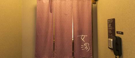 A bathroom with a purple shower curtain, a telephone, and a sign with Japanese characters.