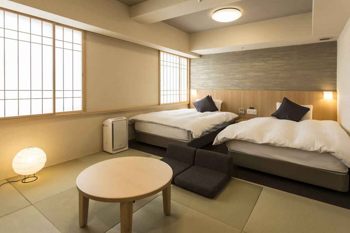 Hotellihuone, jossa on kaksi sänkyä, pyöreä pöytä ja perinteinen japanilaistyylinen lamppu.