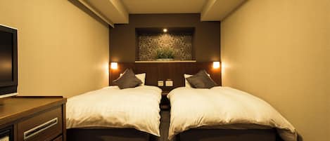 Une chambre d’hôtel avec deux lits, une télévision, une étagère fixée au mur agrémentée d’une plante et un motif décoratif sur le mur.