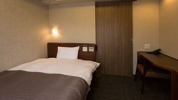 A hotel room with a bed, a desk, and a door.