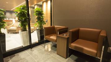 A modern reception area with leather sofas, a wooden side table, and potted plants.