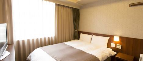 A hotel room with a large bed, a bedside table, a TV, and a window with curtains.