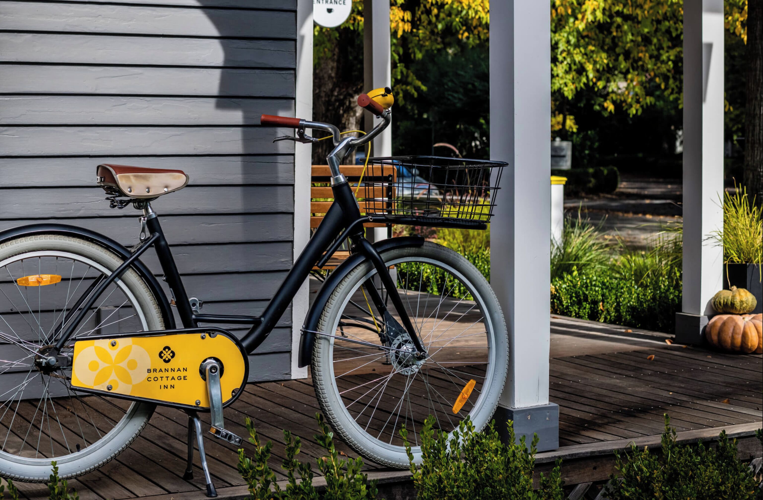 A bicycle with a basket and a yellow sign labeled "Brannan Cottage Inn" on a wooden deck.