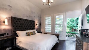 Un dormitorio con una cama grande, cabecera oscura, dos lámparas de noche y vistas a zonas verdes por la ventana.