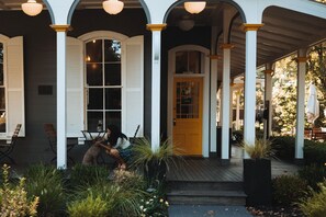 Relax on the covered porch, surrounded by lush greenery, with a table and chairs for outdoor dining or relaxation.