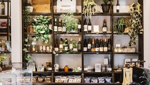 Una zona de bar con estantes llenos de botellas y plantas, una barra con aperitivos y armarios de madera.