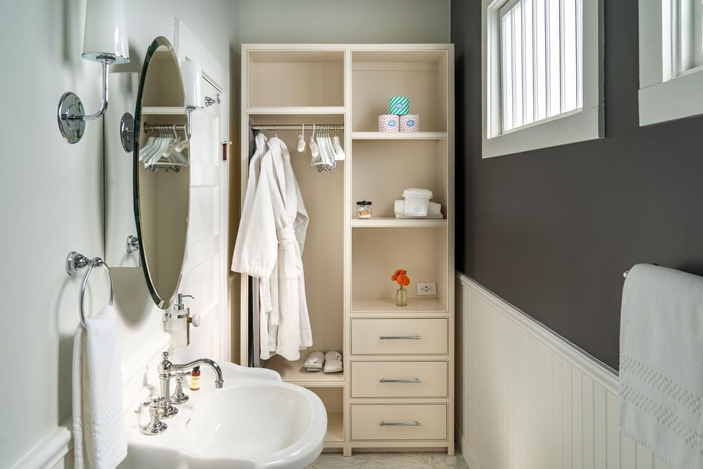 Une salle de bain avec un lavabo blanc, un miroir et un porte-serviettes. On y trouve également un meuble de rangement avec des étagères et des tiroirs.