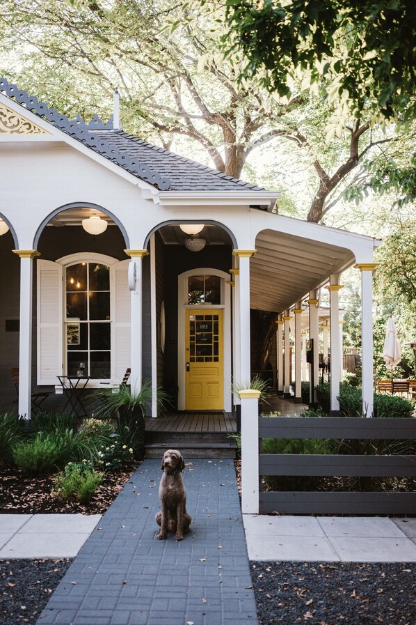 A house with a yellow door and white columns, a dog sitting in front, and a covered porch area. - Brannan Cottage Inn (Calistoga)