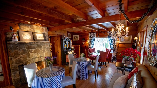 A cozy cabin interior with a stone fireplace, striped tables, and a chandelier.